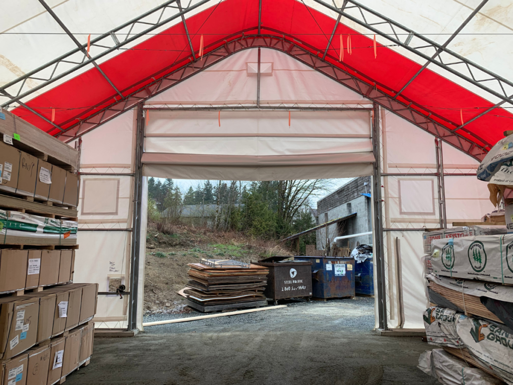 Inside view of a covered storage shelter at Windsor Plywood, showing stacked building materials and weather-resistant fabric structure.
