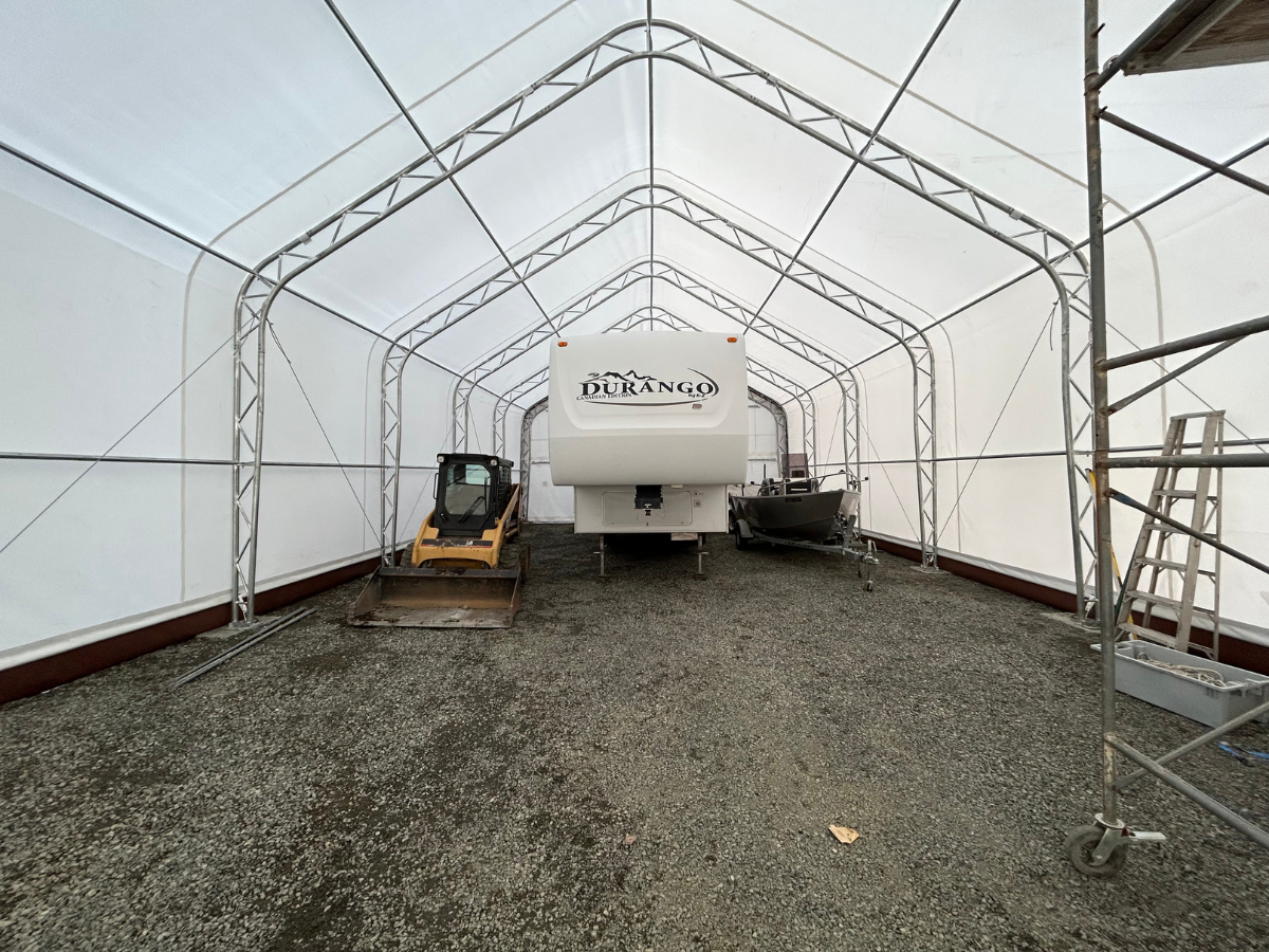 Spacious 30' wide dual-truss fabric shelter with a 16' high peak, housing a Durango RV, a skid steer, and a boat, showcasing ample storage space.